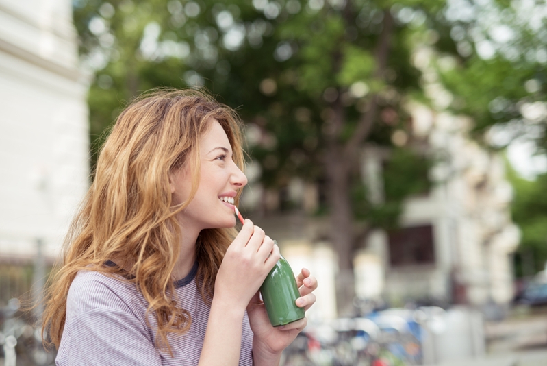 Woman drinking a green smoothie outside.