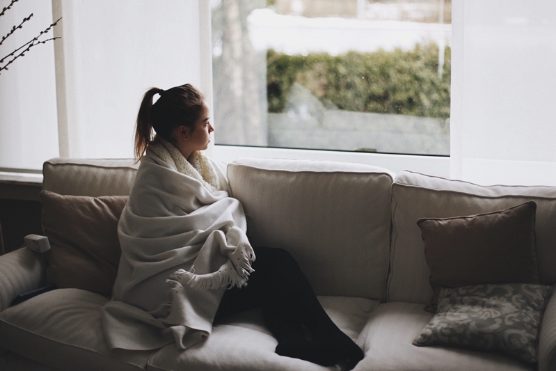 Woman wrapped in blanket looking out the window.